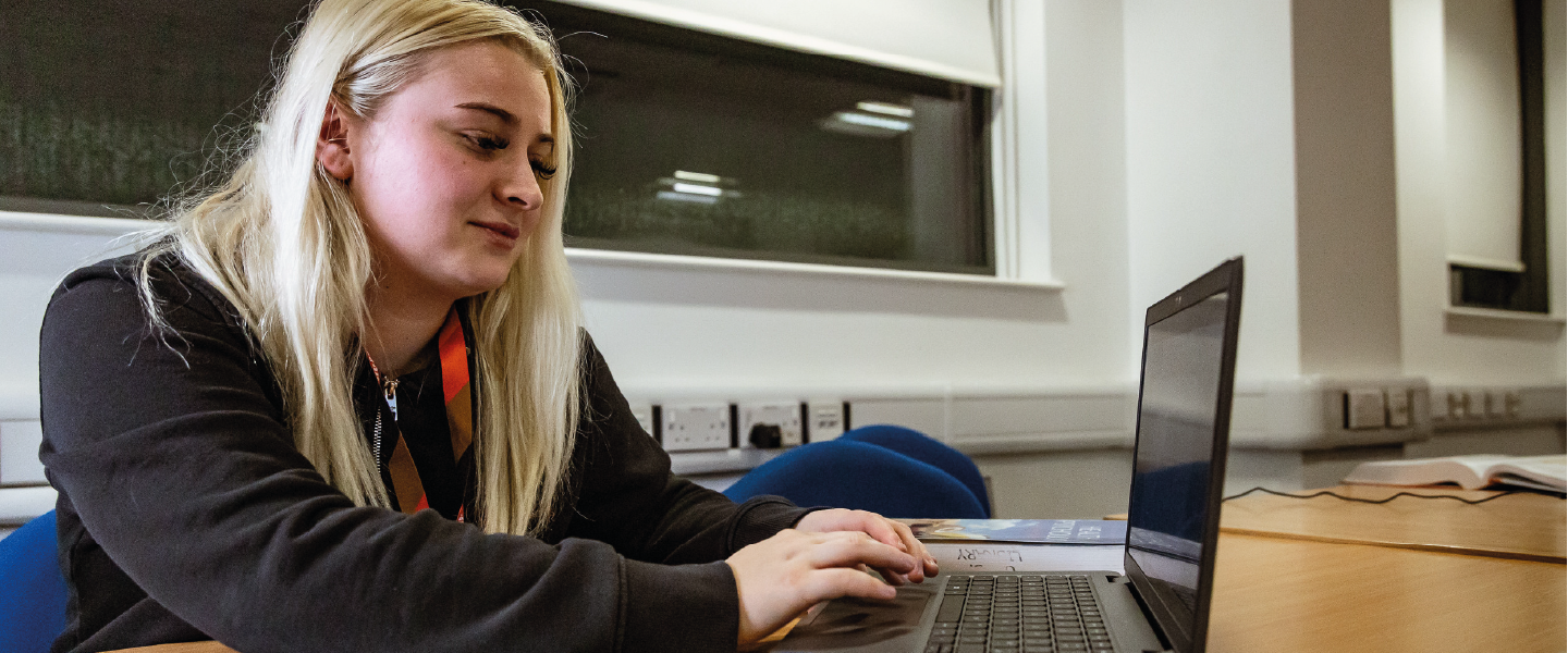 student with blond hair smiling looking at a laptop