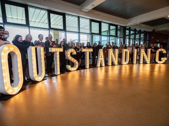 A large group of people posing with large light-up letters that spell the word 'outstanding'