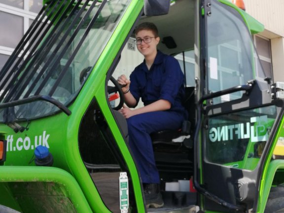 Isabelle Goddard, dressed in blue overalls, sitting in a green tractor
