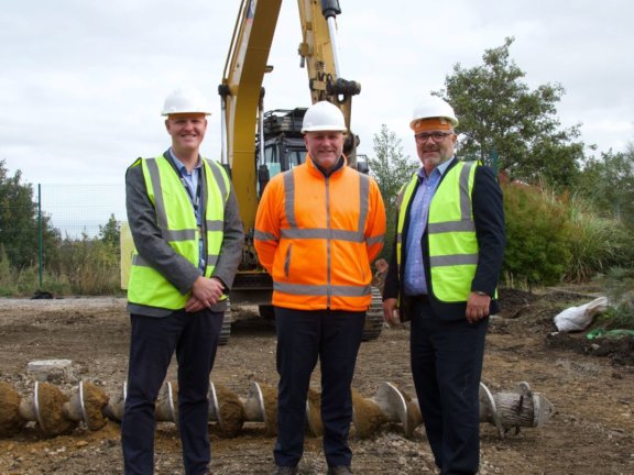 three people in a field in front of a digger machine in hi-vis jackets