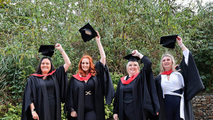 Four people wearing graduation gowns with hats in their left hands