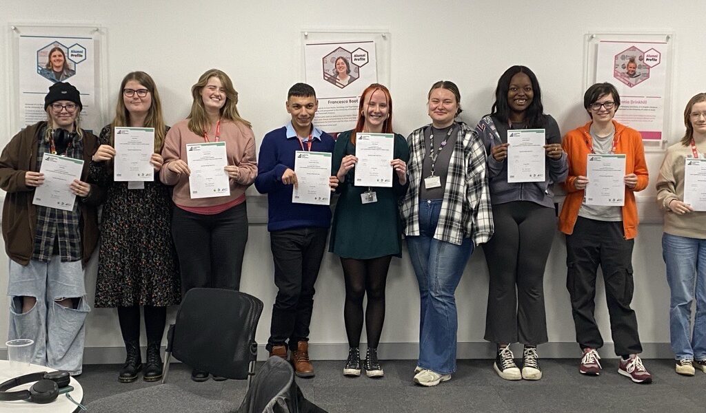 Students celebrate their success on the Environment Leaders Programme. They stand in a classroom in a line, holding certificates.