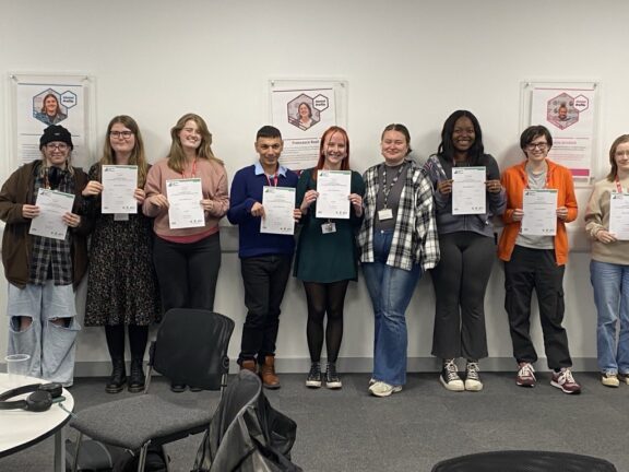 Students celebrate their success on the Environment Leaders Programme. They stand in a classroom in a line, holding certificates.