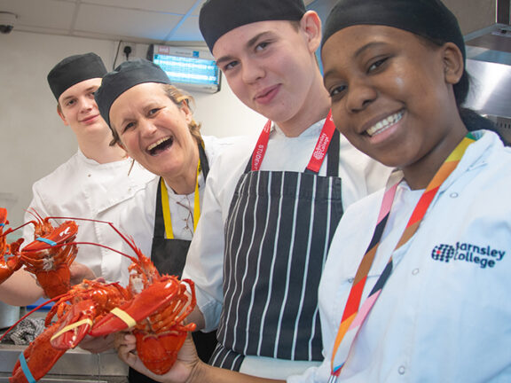 Students smiling at the camera holding cooked lobsters.